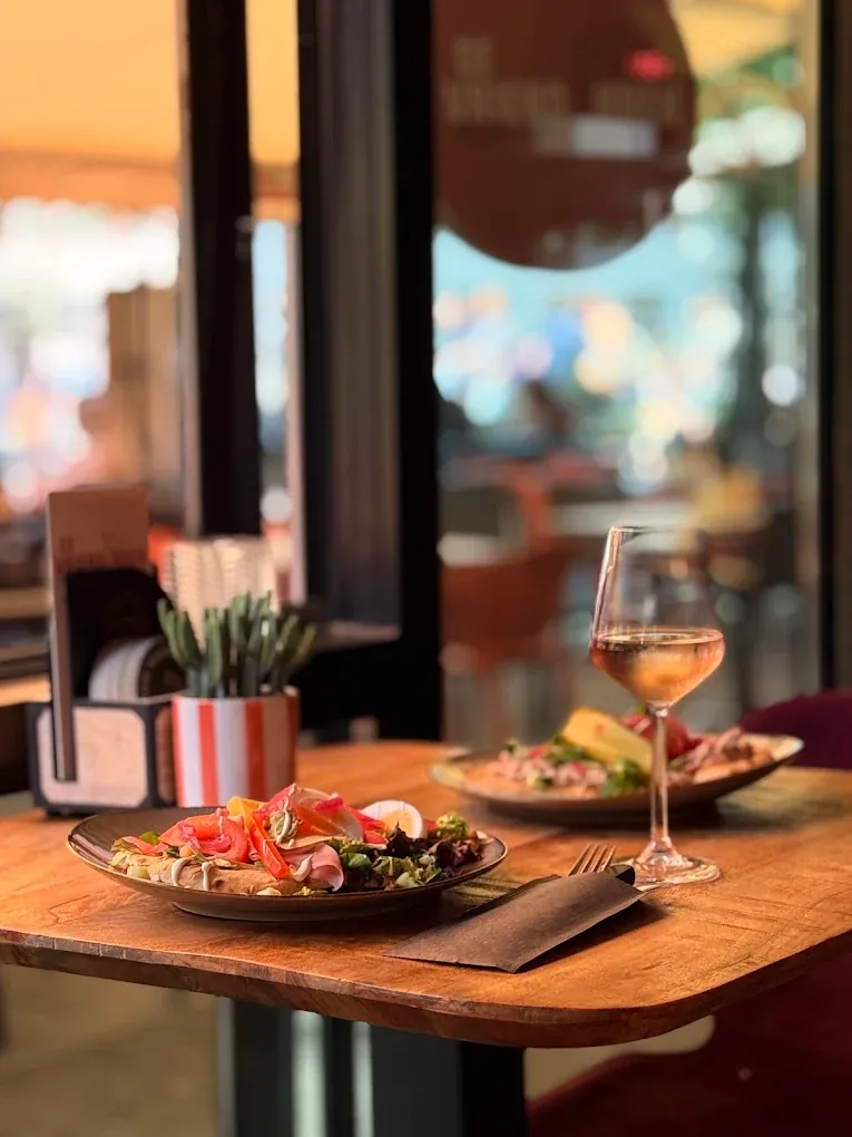 Een tafel bij het raam met een salade en een glas rosé